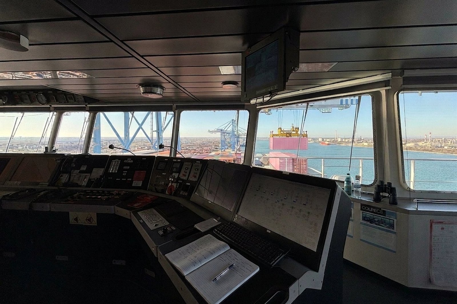 Passerelle de navigation d’un porte-conteneurs : pupitre face au bassin et conteneur suspendu au portique